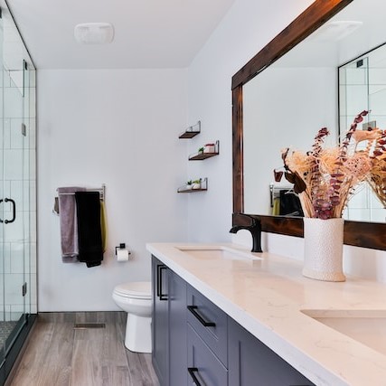 Pristine bathroom with white walls, blue cabinets a glass shower and large mirror with dark wood frame