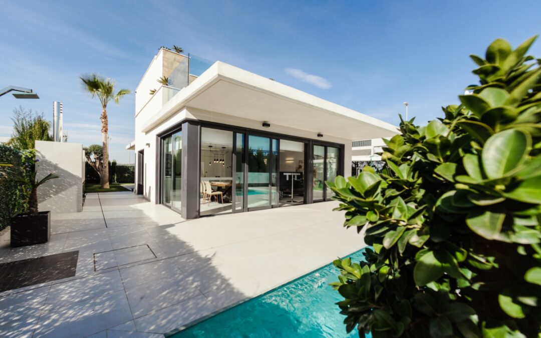 White modern home with full length sliding glass doors opening up to a pool with palm trees in the background