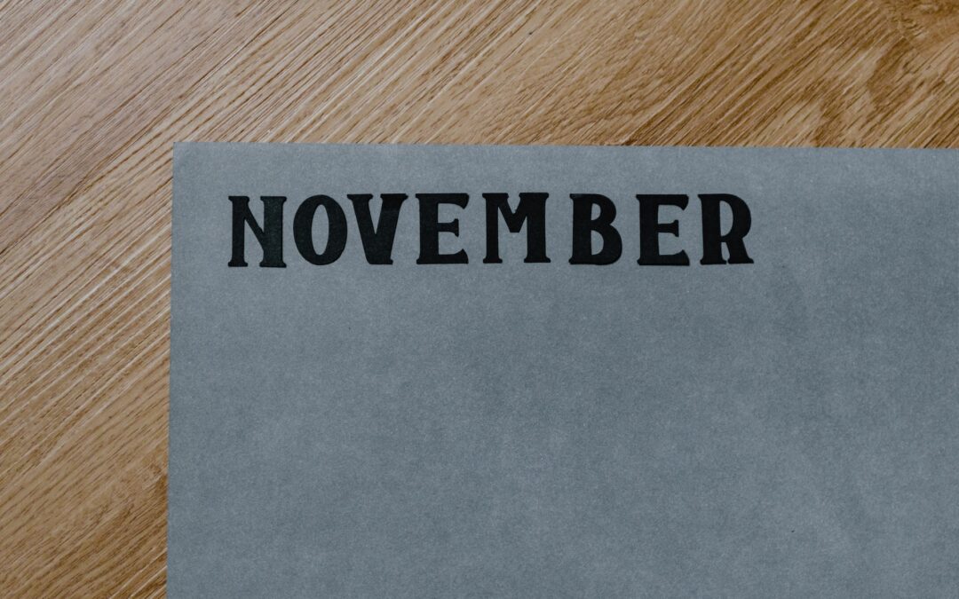 Thick black block letters reading "November" on grey textured paper on a wood desk